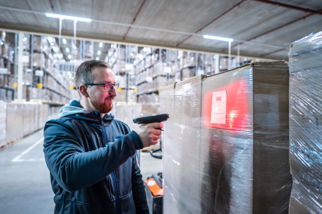 Un homme scanne des colis à l'intérieur d'un entrepôt.